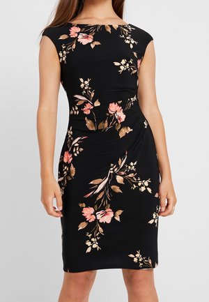 Mouwloze zwarte aansluitende jurk met roze en beige bloemenprint en subtiele zijscheurring, gedragen door een vrouw met lang haar.