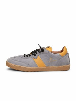 Zapatilla de ante gris con una franja y detalles de cuero color mostaza, cordones negros y suela de goma color caramelo, mostrada de perfil.