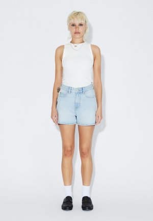 Top blanco sin mangas, pantalones cortos de mezclilla azul claro, zapatos negros y calcetas blancas. Diseño minimalista con un ajuste casual y detalles sutiles.