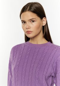 Maglione a maglia cable color viola con scollatura rotonda, motivi testurizzati e finitura in tessuto morbido, indossato da un modello su uno sfondo neutro.