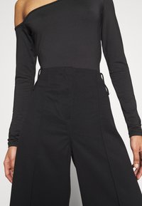 Czarna bluzka z odkrytymi ramionami i długim rękawem o dopasowanym kroju, zestawiona z czarnymi spodniami o wysokim stanie z żeberkową teksturą i wiązaniami po bokach.