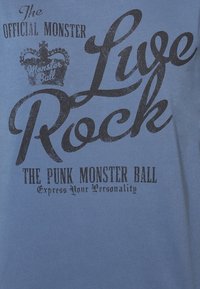 Modrá bavlněná tričko s černým potiskem textu: "Oficiální Monster Ball Live Rock" a "Punk Monster Ball" s grafickým detailem koruny.