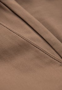 Tissu marron texturé présentant une finition tissée, avec des coutures visibles soulignant les coutures et une surface lisse, légèrement réfléchissante.