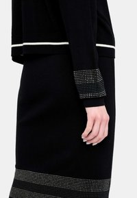 Completo in maglia nera composto da un top con bordi bianchi e una gonna arricchita da borchie metalliche all'orlo. Texture liscia e design aderente.