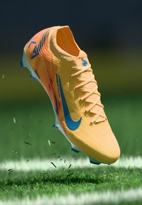 Orangene Fußballschuhe mit einer strukturierten Oberseite, blauen Akzenten und Schnürsenkeln. Sie verfügen über ein schlankes Design und eine leichte Bauweise, die über dem Gras schwebt.