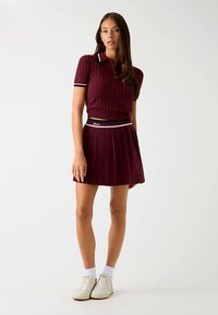 Burgundy pleated skirt with matching ribbed polo, featuring white and navy accents, paired with white sneakers and crew socks.