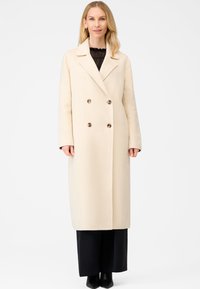 Beige dobbeltbrystet frakke med notch-krave, lavet af blødt stof, med store runde knapper og en lige silhuet.