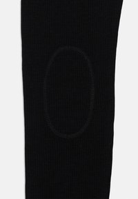 Fekete bordázott leggings, amely textúrált anyagból készült, és jellegzetes ovális térdpanellel rendelkezik, amely növeli a tartósságot és a dizájn részletességét.