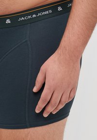 Dunkelblaue Boxer-Shorts mit einem elastischen Bund, auf dem "JACK & JONES" in Weiß und Gold steht. Glatte Stoffqualität mit eng anliegender Passform.