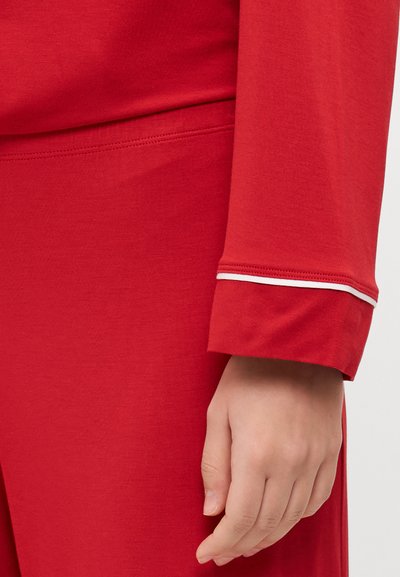 Red long-sleeve garment with a smooth texture, featuring a cuff trimmed in white. Fabric appears soft and lightweight, ideal for relaxed wear.