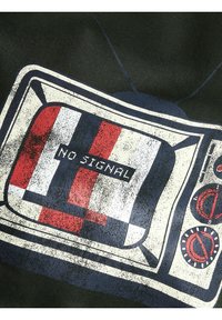 Grafisk trykk av et retro-tv med meldingen «INGEN SIGNAL». Har røde, hvite og blå farger, med knotter og en slitt tekstur.