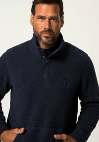 Pullover in fleece blu navy con colletto alto, dotato di patta con bottoni, superficie testurizzata e logo stampato sul petto.
