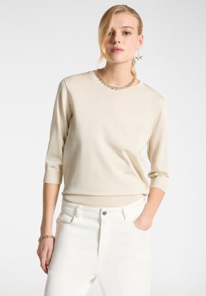 Maglione leggero beige a maglia con maniche a tre quarti e orlo a costine, abbinato a pantaloni bianchi. Presenta un colletto decorativo.
