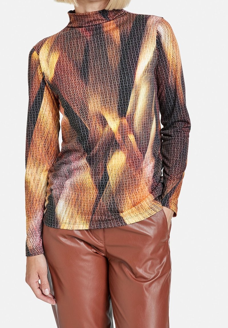T-shirt à manches longues avec un col haut, présentant un motif géométrique aux teintes orange, marron et noir sur un tissu texturé.