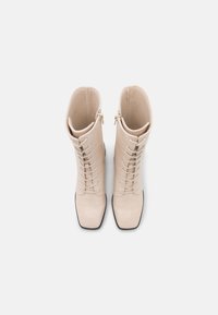 Beige Kunstleder kniehohe Stiefel mit Krokodilprägung, quadratischer Zehenform, Schnürung vorne und seitlichem Reißverschluss.