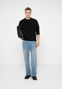Suelto de punto negro, vaqueros rectos azul claro y zapatos de cuero negros. Sosteniendo un bolso de cuero negro. Atuendo simple y casual.