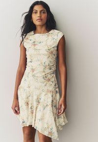 Ein blütenmusterndes Kleid mit einem weichen cremefarbenen Grundton, tailliertem Oberteil, kurzen Ärmeln und einem ausgestellten, asymmetrischen Saum. Strukturierter Stoff mit leichtem Raffung.