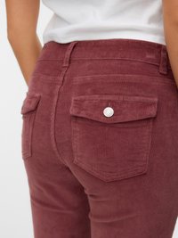 Baršunaste hlače u maroon boji s izraženom rebrastom teksturom, dva stražnja džepa s preklopima i metalna dugmad na pojasu.