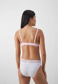 Lichtroze beha met verstelbare bandjes en een haaksluiting, gecombineerd met een witte slip met een kantaccent in de tailleband. Glad textuur van de stof.