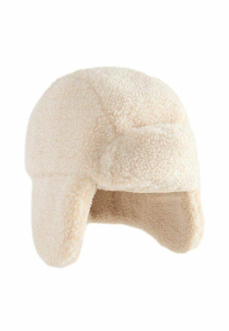 Cappello da trapper in finta pelliccia color crema; parte superiore rotonda, paraorecchie e tessuto testurizzato. Design semplice, materiale morbido e caldo.