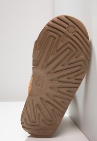 UGG-såle i brunt gummi, med et zigzag-mønster og sirkelformet logo. Glatt tekstur med hevede detaljer for bedre grep.