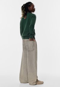 Zielony sweter z dzianiny i obszerne, jasnoszare dżinsowe spodnie z dużymi kieszeniami. Slim fit u góry, rozszerzające się u dołu. Teksturowany materiał.