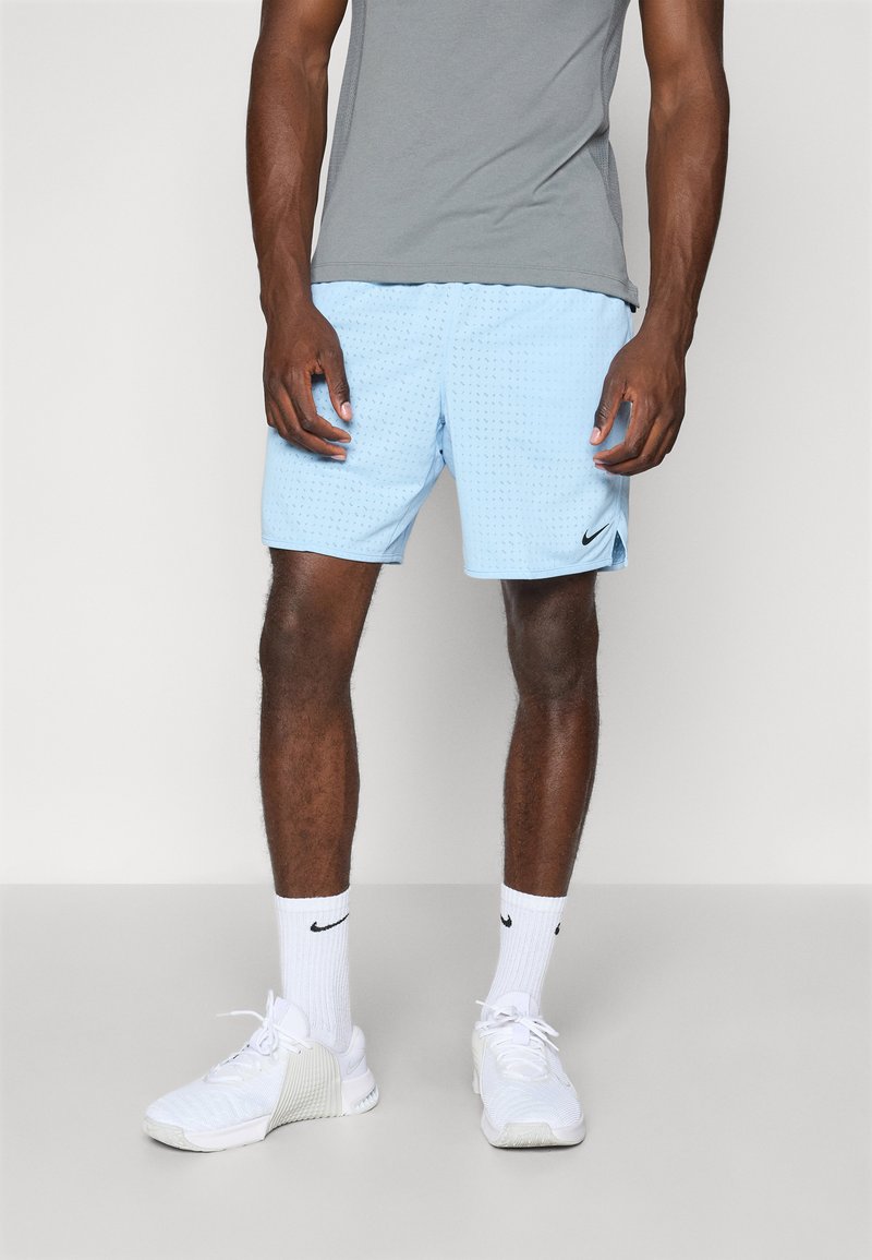Light blue athletic shorts with textured design, worn with a gray shirt and white sneakers. Nike logo on shorts and socks.