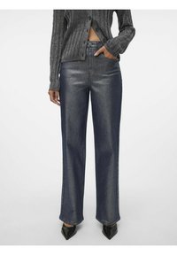 Jeans a vita alta in denim scuro con un effetto metallico, vestibilità ampia e cuciture dettagliate, abbinati a un top grigio a maniche lunghe con texture.