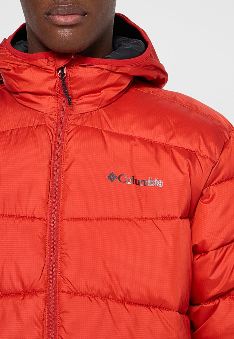 Chaqueta acolchada aislante roja con capucha, con cierre frontal y diseño acolchado horizontal. Logo de Columbia en el lado izquierdo del pecho.