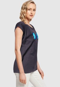 Mørk grå t-skjorte med korte, rullet ermene, med et blått sommerfuglgraphic på forsiden. Laget av mykt bomullsmateriale.