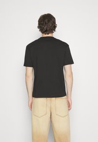 T-shirt en coton noir, à manches courtes, col rond, texture lisse. Porté avec un pantalon large taille haute beige clair doté de poches arrière.