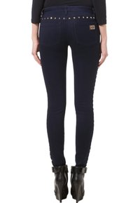 Jeans ajustados de denim azul oscuro con acentos de tachuelas en la cintura. Diseño entallado con bolsillos traseros y textura ligeramente desgastada.