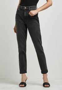 Höga svarta denimjeans med rak passform, uppvikt fåll och guldhardware vid midjan. Slät textur och klassisk design.