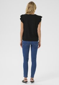 Haut noir à manches courtes et volantées, avec un motif à œillets. Assorti à un jean bleu slim et des sandales noires.