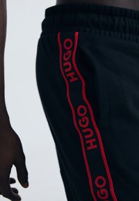 Zwarte joggers met een rode 'HUGO' logo-stripe langs de zijkant, gemaakt van zacht materiaal met een elastische tailleband.