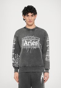 Siva majica s kapuco z belo grafiko pajkove mreže. Ima okrogel vrat, dolge rokave in rebraste manšete. Podroben sprednji dizajn.