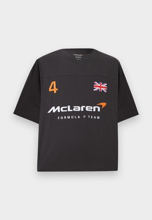 Μαύρο πουκάμισο με κοντά μανίκια και V-λαιμόκοψη, με πορτοκαλί αριθμό 4, σημαία του Ηνωμένου Βασιλείου και λευκό λογότυπο της ομάδας McLaren Formula 1 στο μπροστινό μέρος.