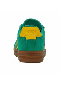 Zielone zamszowe sneakersy K-Swiss z żółtą klapką na pięcie i brązową gumową podeszwą, widziane z tyłu na białym tle.