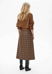 Bruine gebreide trui gecombineerd met een bruine geruite maxi rok met donkere en lichte beige accenten, gedragen met zwarte kniehoge laarzen.