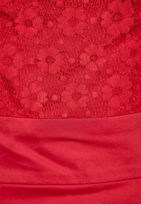 Robe rouge avec une partie supérieure en dentelle florale texturée et une partie inférieure en satin lisse, mettant en avant des motifs floraux complexes et une silhouette ajustée.