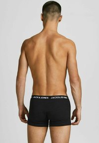 Schwarze Boxershorts mit einem elastischen Bund, der mit "JACK & JONES" in weißer Schrift bedruckt ist, von hinten auf einem nackten Oberkörper betrachtet.