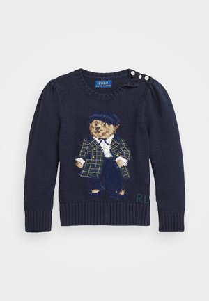 Marineblå strikket sweater med en bjørn iført ternet jakke, hvid skjorte og marineblåt kasket, med knaplukning på skulderen og initialerne "RL".