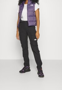 Fioletowa ocieplana kamizelka na białej koszulce, w połączeniu z czarnymi spodniami typu cargo i czarnymi trampkami z fioletowymi akcentami.