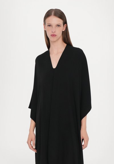 Svart, flödande kaftan med V-krage och vida ärmar. Tillverkad av mjukt tyg med en slät struktur och minimalistisk design.