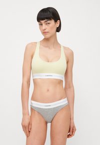 Lys gul ribbet bralette med bred hvit kant og logo; grå bomullsbikini undertøy med hvit midje og logo.