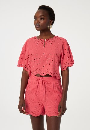 Koraalroze katoenen set met een top met scalloped zoom en bloemen oogjes-details, en bijpassende shorts met soortgelijke patronen en een strik taille.