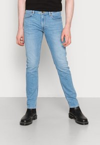 Ljusblå skinny jeans i denim med klassisk fem-fickorsdesign, med dragkedja och bärs med svarta läderankelstövlar.