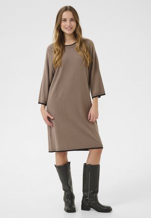 Brown knit dress with 3/4 sleeves, black trim at neckline and hem, knee-length. Paired with knee-high black leather boots.