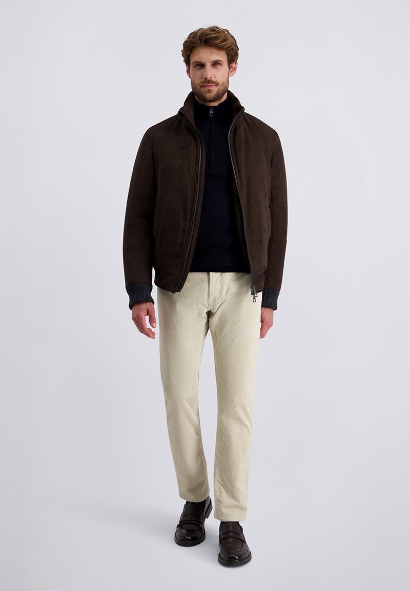 Brown suede jacket with a zip collar, ribbed cuffs, layered over a navy zip turtleneck, paired with light beige corduroy pants. Brown shoes.