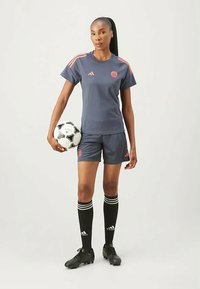 Tume sinine jalgpalli vorm, millel on oranžid aktsendid, sisaldab lühikeste varrukatega särki, lühikesi pükse, põlve pikkuseid musti soku ja musti jalgpalle.